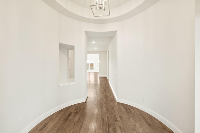 corridor with a chandelier, wood finished floors, and baseboards