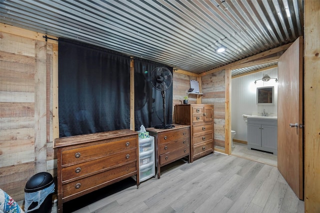 bedroom featuring wood walls, ensuite bathroom, light hardwood / wood-style floors, and sink