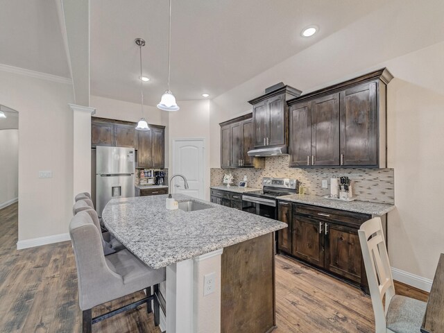 kitchen with hardwood / wood-style floors, a center island with sink, hanging light fixtures, decorative backsplash, and appliances with stainless steel finishes