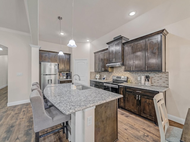 kitchen with tasteful backsplash, decorative light fixtures, a center island with sink, stainless steel appliances, and light stone countertops