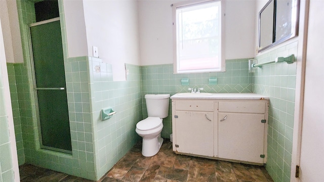 bathroom with vanity, a shower with shower door, toilet, and tile walls