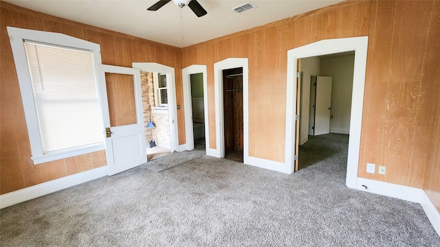 unfurnished bedroom with carpet floors, wooden walls, a closet, and ceiling fan