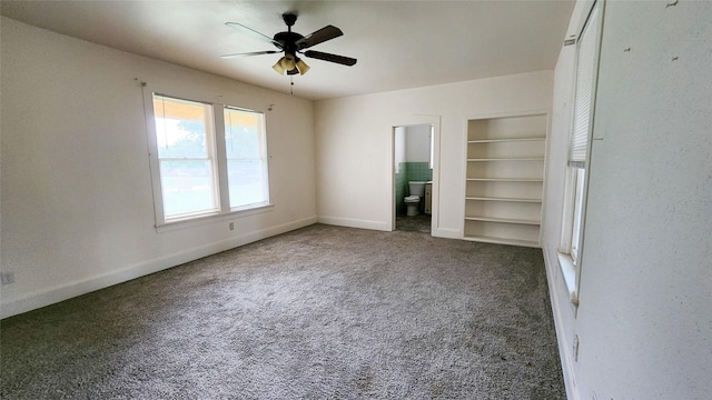 unfurnished bedroom with ceiling fan, ensuite bath, and dark colored carpet