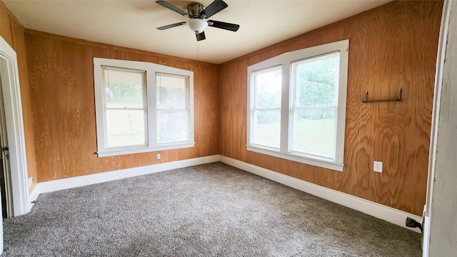 carpeted empty room featuring ceiling fan and wood walls