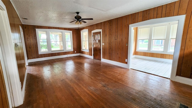 interior space with ceiling fan, a textured ceiling, dark hardwood / wood-style flooring, and wood walls