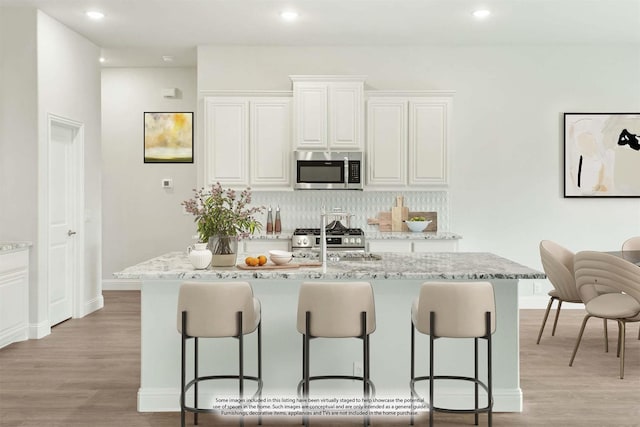 kitchen featuring light wood-type flooring, stainless steel appliances, white cabinetry, and an island with sink