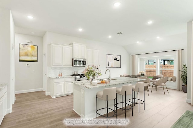 kitchen with light stone counters, stainless steel appliances, a kitchen island with sink, light hardwood / wood-style flooring, and white cabinets