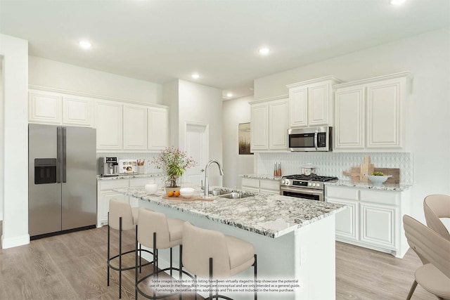 kitchen featuring appliances with stainless steel finishes, backsplash, sink, white cabinetry, and an island with sink