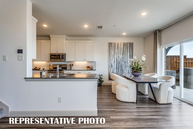 kitchen with decorative backsplash, white cabinetry, hardwood / wood-style floors, and stainless steel appliances