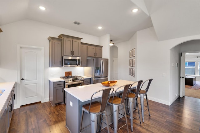 kitchen featuring a breakfast bar, a center island, dark wood-type flooring, vaulted ceiling, and stainless steel appliances