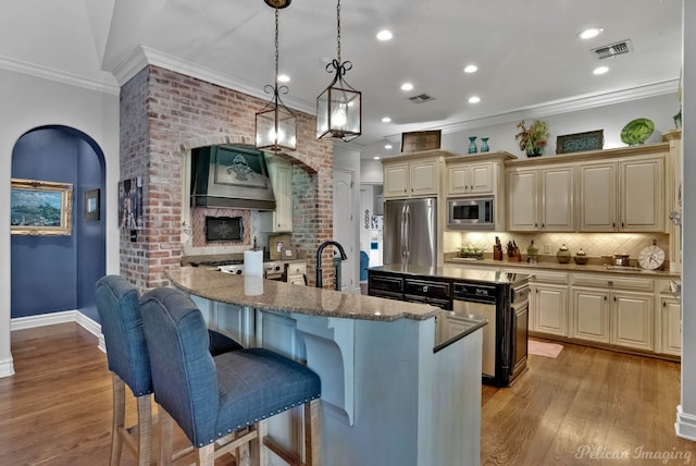 kitchen with pendant lighting, a kitchen bar, an island with sink, and appliances with stainless steel finishes