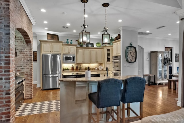 kitchen with pendant lighting, hardwood / wood-style flooring, appliances with stainless steel finishes, a kitchen island with sink, and light stone countertops