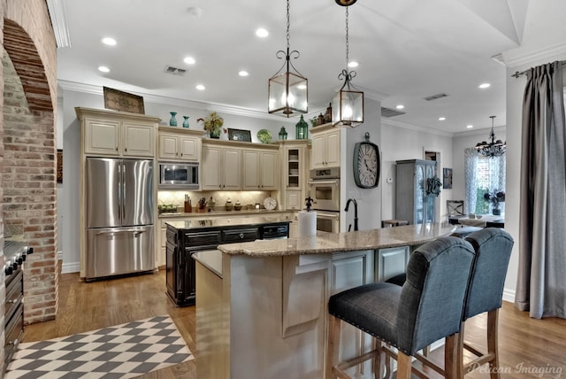 kitchen featuring appliances with stainless steel finishes, a kitchen island with sink, pendant lighting, and cream cabinetry