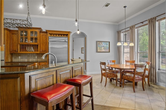 kitchen featuring decorative backsplash, dark stone counters, crown molding, built in refrigerator, and hanging light fixtures