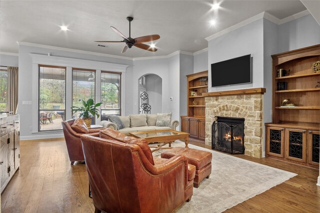 living room featuring a stone fireplace, crown molding, ceiling fan, and light hardwood / wood-style floors