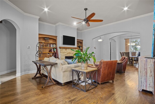 living room featuring hardwood / wood-style flooring, ceiling fan with notable chandelier, ornamental molding, and a fireplace