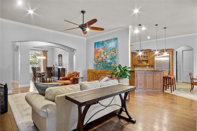 living room with ceiling fan with notable chandelier, light hardwood / wood-style floors, ornamental molding, and sink