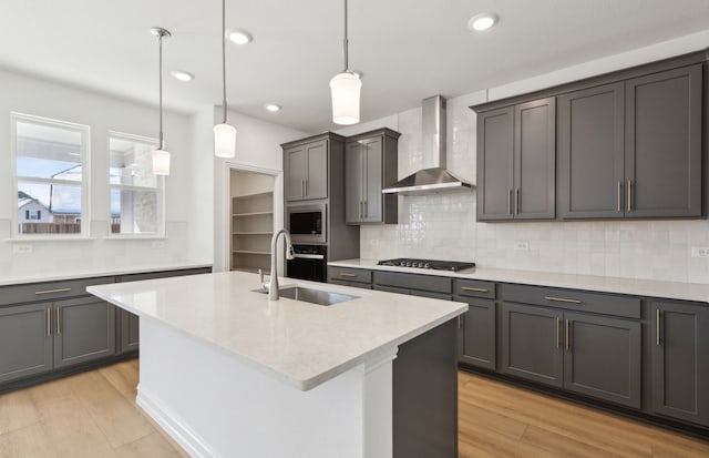 kitchen featuring appliances with stainless steel finishes, an island with sink, sink, hanging light fixtures, and wall chimney exhaust hood