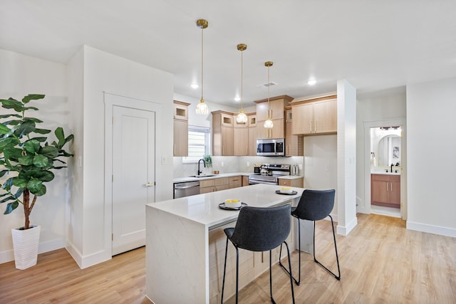 kitchen featuring hanging light fixtures, a center island, stainless steel appliances, light brown cabinets, and light wood-type flooring