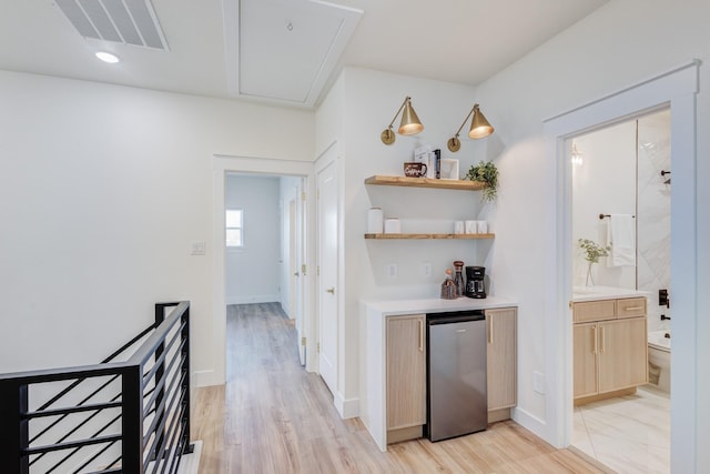 bar with stainless steel fridge, light brown cabinetry, and light hardwood / wood-style flooring