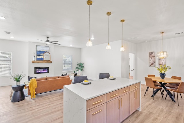 1724 S Hughes Ave, Fort Worth, TX 76105 - kitchen featuring light wood-style flooring, hanging light fixtures, a ceiling fan, a kitchen island, and a glass covered fireplace
