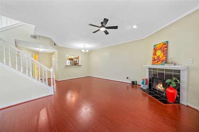 living room featuring hardwood / wood-style floors, ceiling fan with notable chandelier, ornamental molding, and a tiled fireplace