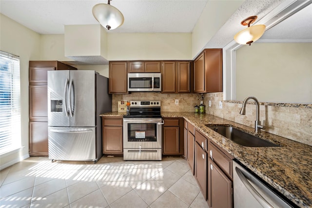 kitchen featuring stone counters, sink, backsplash, light tile patterned flooring, and appliances with stainless steel finishes