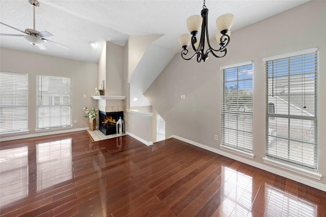 unfurnished living room featuring lofted ceiling, dark hardwood / wood-style floors, a textured ceiling, a tiled fireplace, and ceiling fan with notable chandelier