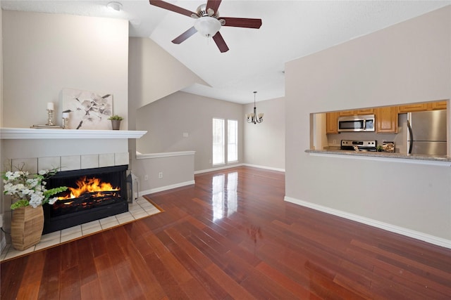 unfurnished living room featuring a tiled fireplace, ceiling fan with notable chandelier, wood-type flooring, and high vaulted ceiling