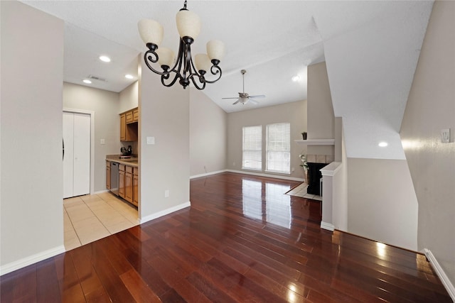 interior space featuring a tile fireplace, vaulted ceiling, ceiling fan with notable chandelier, stainless steel dishwasher, and light hardwood / wood-style floors