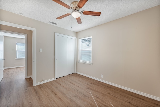 unfurnished bedroom with ceiling fan, light hardwood / wood-style floors, a textured ceiling, and multiple windows