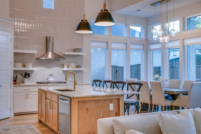 kitchen with a center island with sink, wall chimney exhaust hood, pendant lighting, and sink