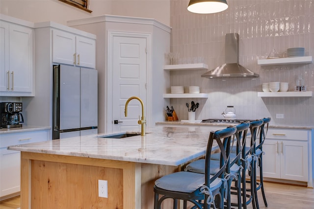 kitchen with sink, refrigerator, white cabinetry, and wall chimney range hood