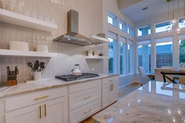 kitchen featuring a wealth of natural light, light stone counters, decorative light fixtures, and wall chimney range hood