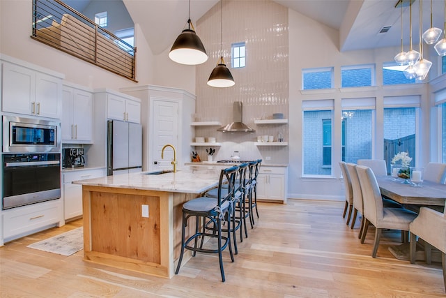 kitchen with stainless steel appliances, sink, high vaulted ceiling, white cabinetry, and an island with sink