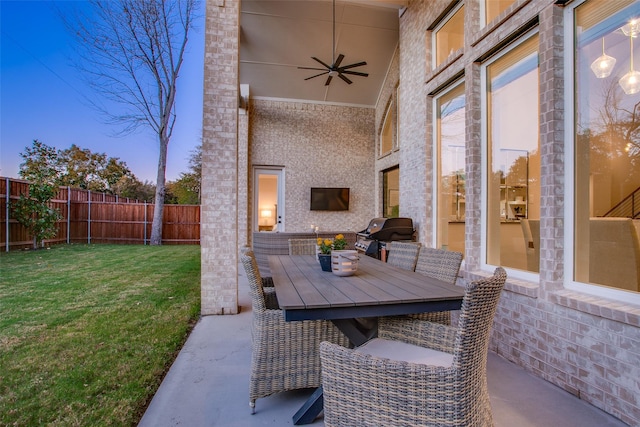 patio terrace at dusk featuring grilling area, ceiling fan, and a yard