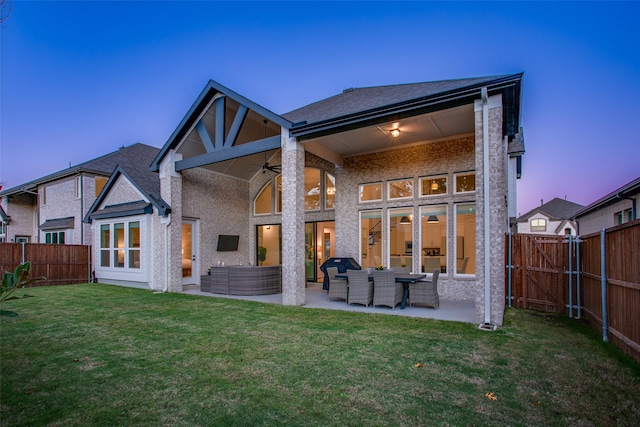 back house at dusk with ceiling fan, a yard, and a patio