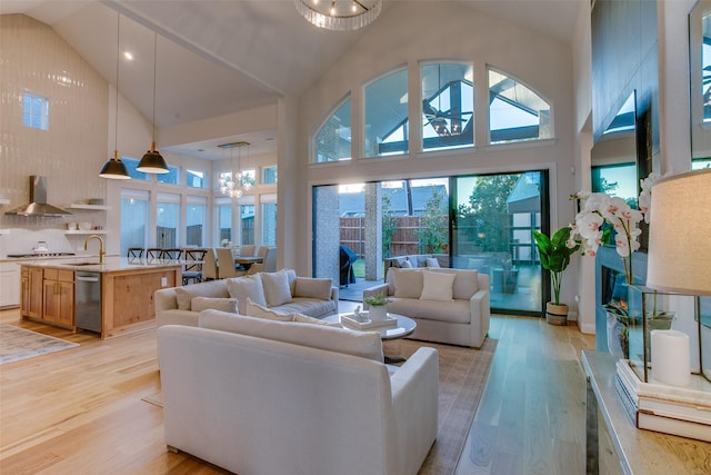 living room featuring a notable chandelier, sink, high vaulted ceiling, and light hardwood / wood-style flooring