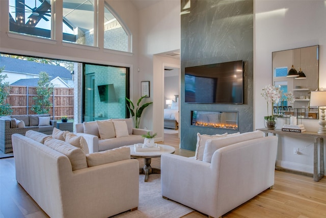 living room with a large fireplace, a towering ceiling, and light hardwood / wood-style floors