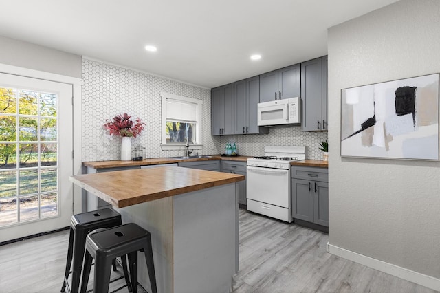 kitchen with gray cabinetry, wooden counters, white appliances, a kitchen bar, and a kitchen island