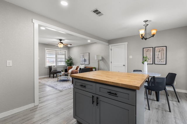 kitchen featuring gray cabinetry, hanging light fixtures, light hardwood / wood-style flooring, wooden counters, and ceiling fan with notable chandelier