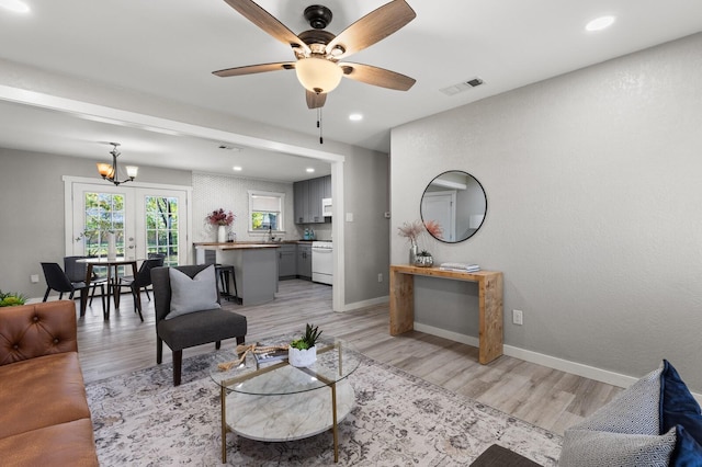 living room with ceiling fan with notable chandelier and light hardwood / wood-style flooring