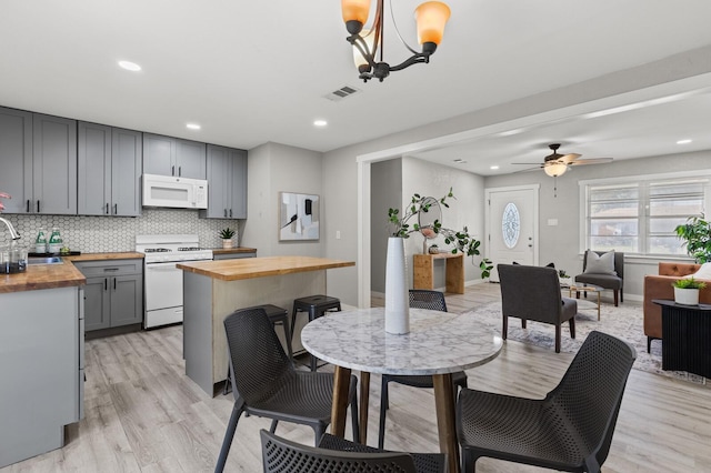 kitchen with gray cabinetry, white appliances, ceiling fan with notable chandelier, light hardwood / wood-style flooring, and butcher block countertops