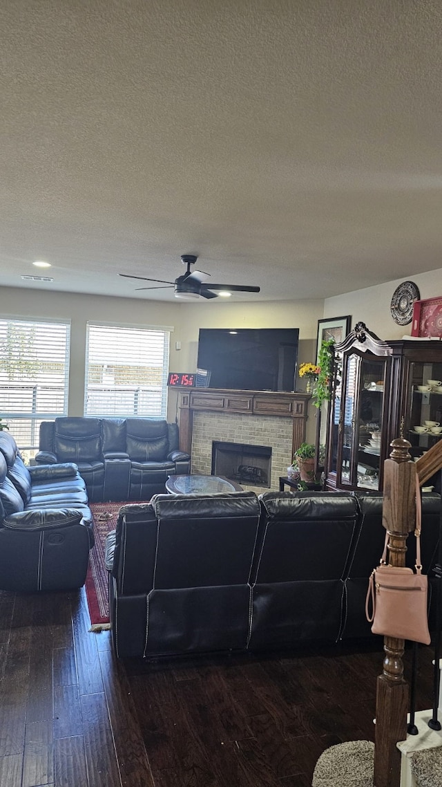 living room featuring a textured ceiling, a stone fireplace, ceiling fan, and dark hardwood / wood-style floors