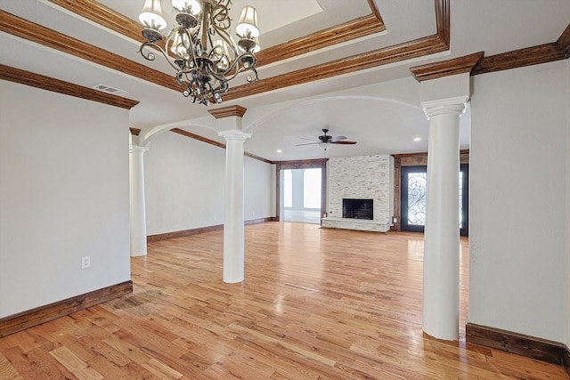 unfurnished living room featuring ceiling fan with notable chandelier, light hardwood / wood-style flooring, ornamental molding, a fireplace, and decorative columns