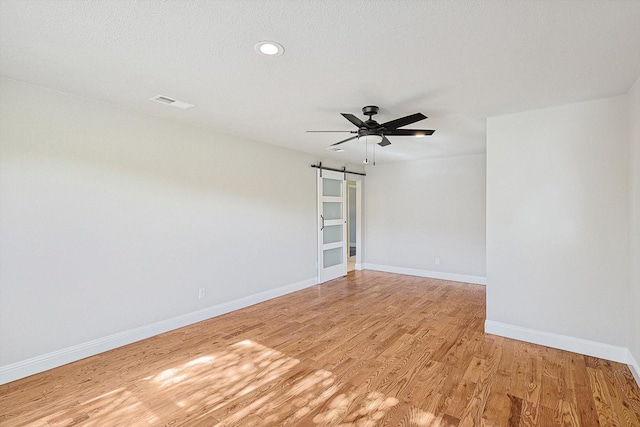 unfurnished room featuring a barn door, ceiling fan, a textured ceiling, and light wood-type flooring