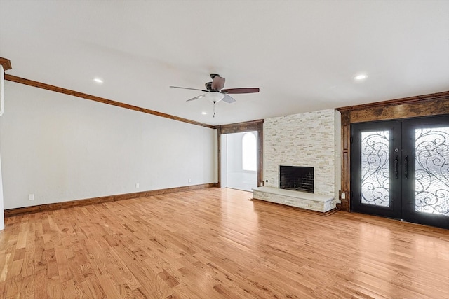 unfurnished living room featuring ceiling fan, a stone fireplace, light wood-type flooring, and french doors