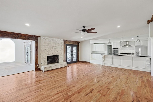 unfurnished living room with lofted ceiling, a stone fireplace, sink, ceiling fan, and light hardwood / wood-style floors