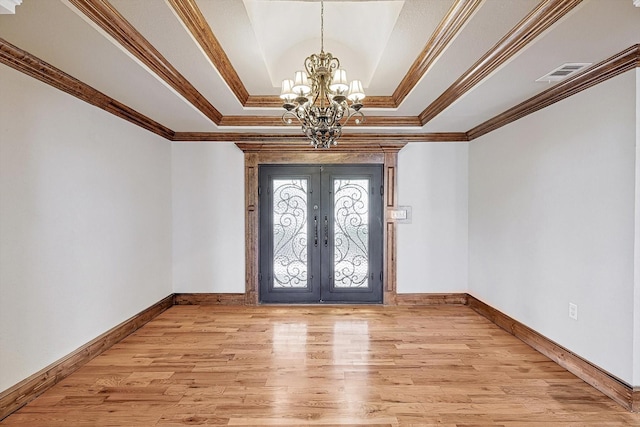 foyer with french doors, light wood-type flooring, a tray ceiling, and a notable chandelier