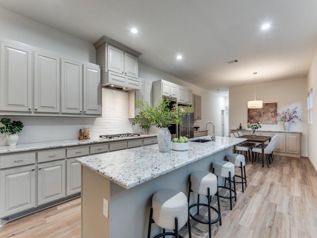 kitchen with a kitchen island with sink, stainless steel appliances, decorative light fixtures, and light wood-type flooring